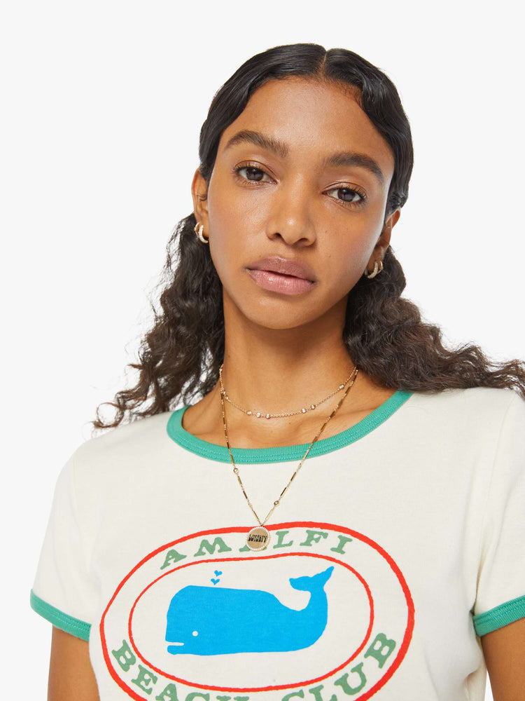 Detailed view of a woman in an off-white shrunken crewneck tee with extra-short sleeves and a cropped hem designed with a blue whale graphic on the front and teal hems.