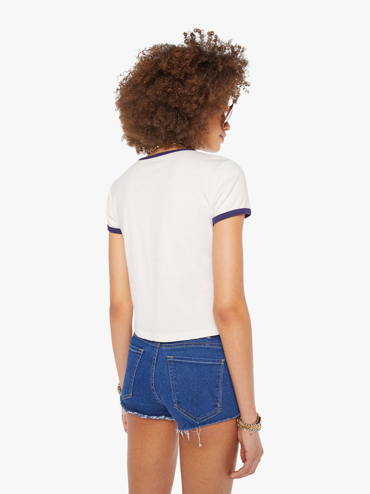 Back view of a woman in a white tee with navy trim and puff print text on the front.