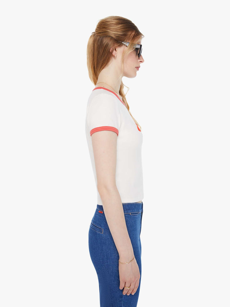 Side view of a woman in a white with faded red trim with an abstract rose graphic crewneck tee with extra-short sleeves and a cropped hem. 