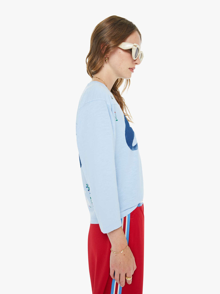 Side view of a woman in a sky blue tee with a 68 in navy on the front and back and colorful hand-drawn doodles throughout.