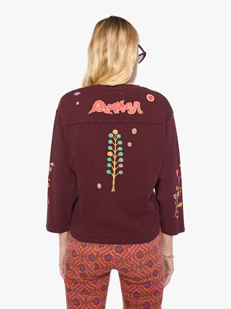 Back view of a woman in a  3/4 sleeves and a boxy fit tee with colorful bird on the front, hand-drawn doodles throughout and MOTHER's name across the back.