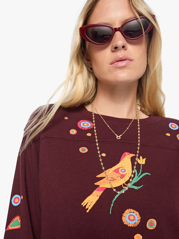 Close up view of a woman in a  3/4 sleeves and a boxy fit tee with colorful bird on the front, hand-drawn doodles throughout and MOTHER's name across the back.