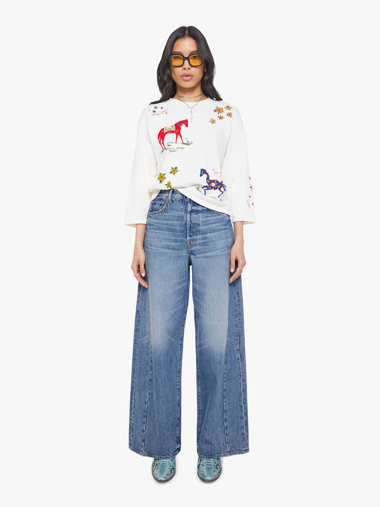Full body view of a woman in horse and flower white oversized crewneck tee is designed with drop shoulders, 3/4 sleeves and a boxy fit.