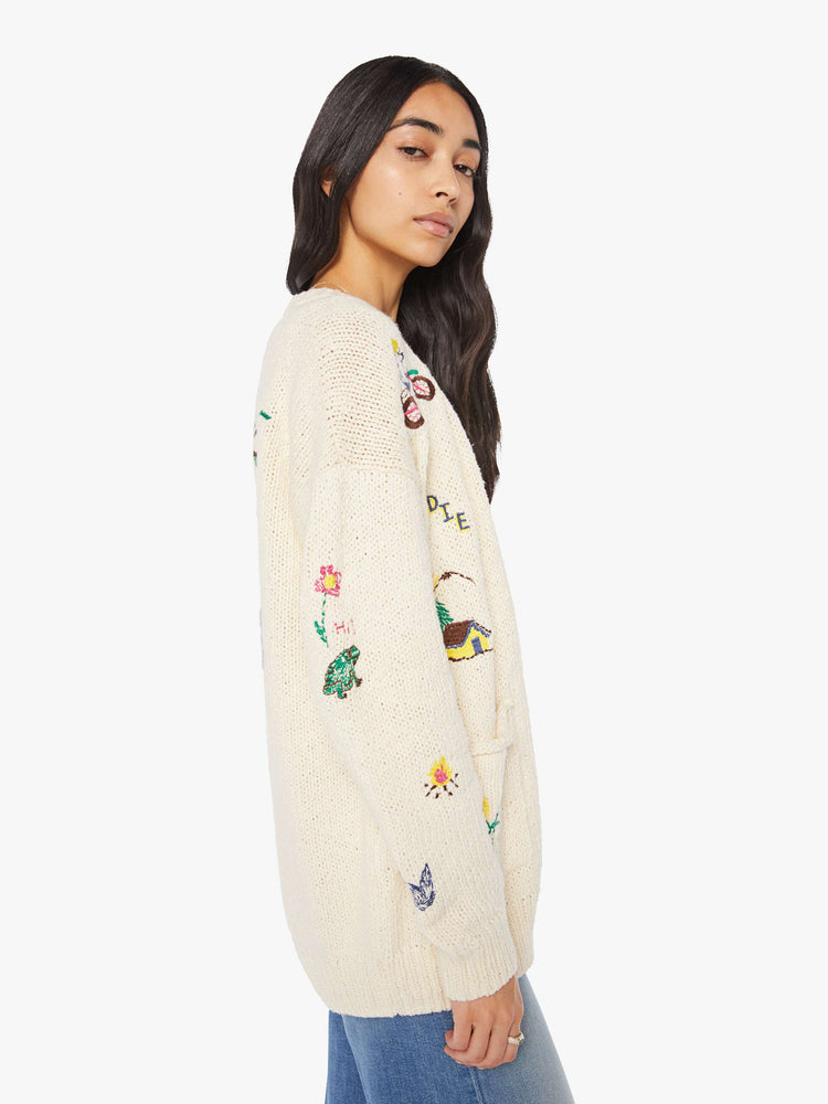 Side view of a woman in a cream with colorful embroidery  oversized crewneck cardigan with drop shoulders, patch pockets and ribbed hems. 