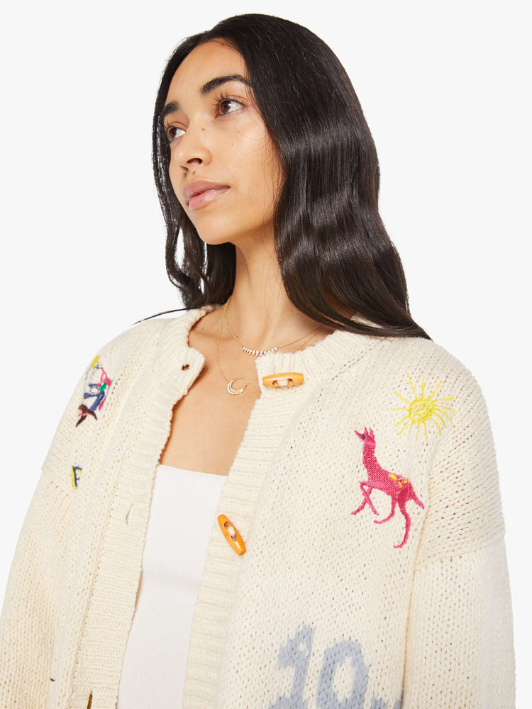 Close up view of a woman in a cream with colorful embroidery  oversized crewneck cardigan with drop shoulders, patch pockets and ribbed hems. 