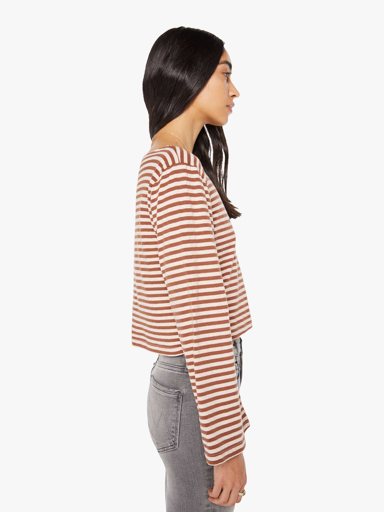 Side view of a woman in horizontal brown and white stripes long sleeve tee with a boat neck and boxy fit.