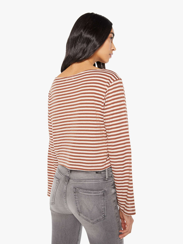 Back view of a woman in horizontal brown and white stripes long sleeve tee with a boat neck and boxy fit.