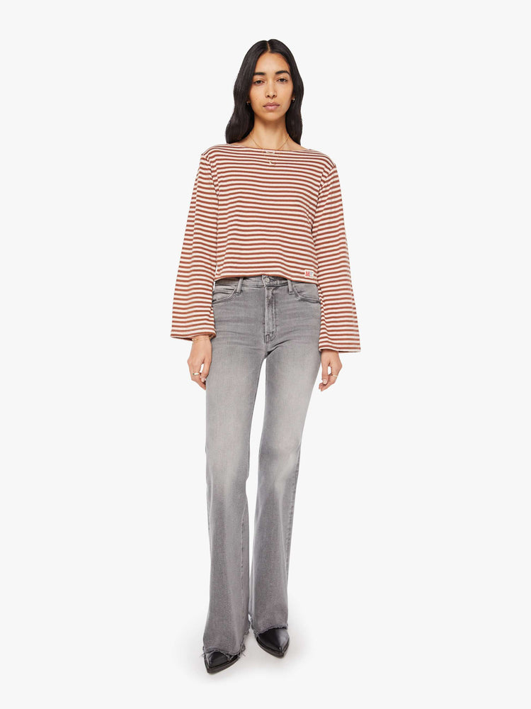 Full body view of a woman in horizontal brown and white stripes long sleeve tee with a boat neck and boxy fit.