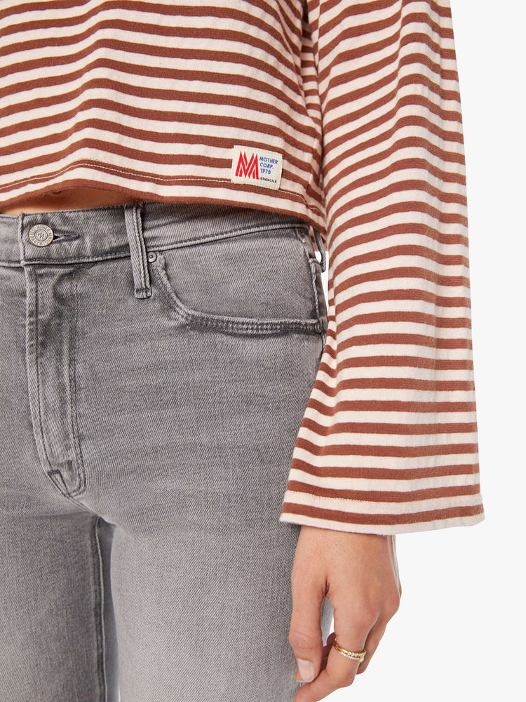 Hem view of a woman in horizontal brown and white stripes long sleeve tee with a boat neck and boxy fit.