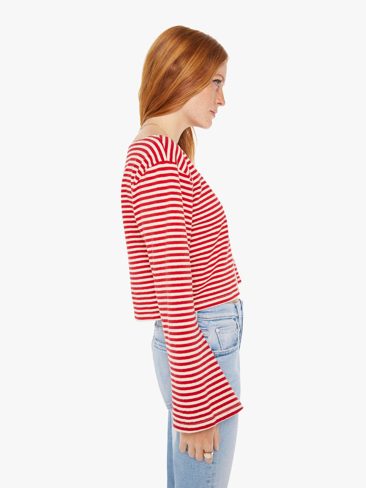 Side view of a woman red and white stripe pattern boatneck top with long sleeves, drop shoulders, a cropped hem and boxy fit.