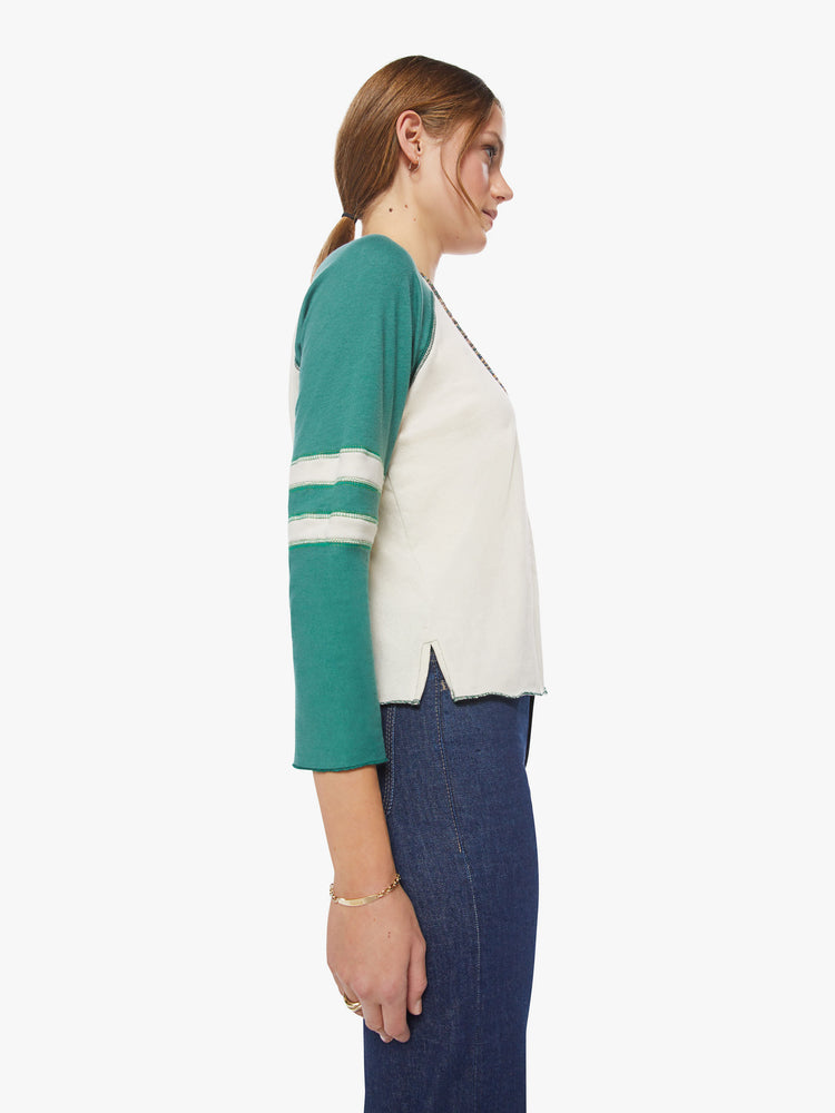 Side view of a woman concert tee designed with a crew neck, 3/4 sleeves in an off-white hue with teal sleeves.