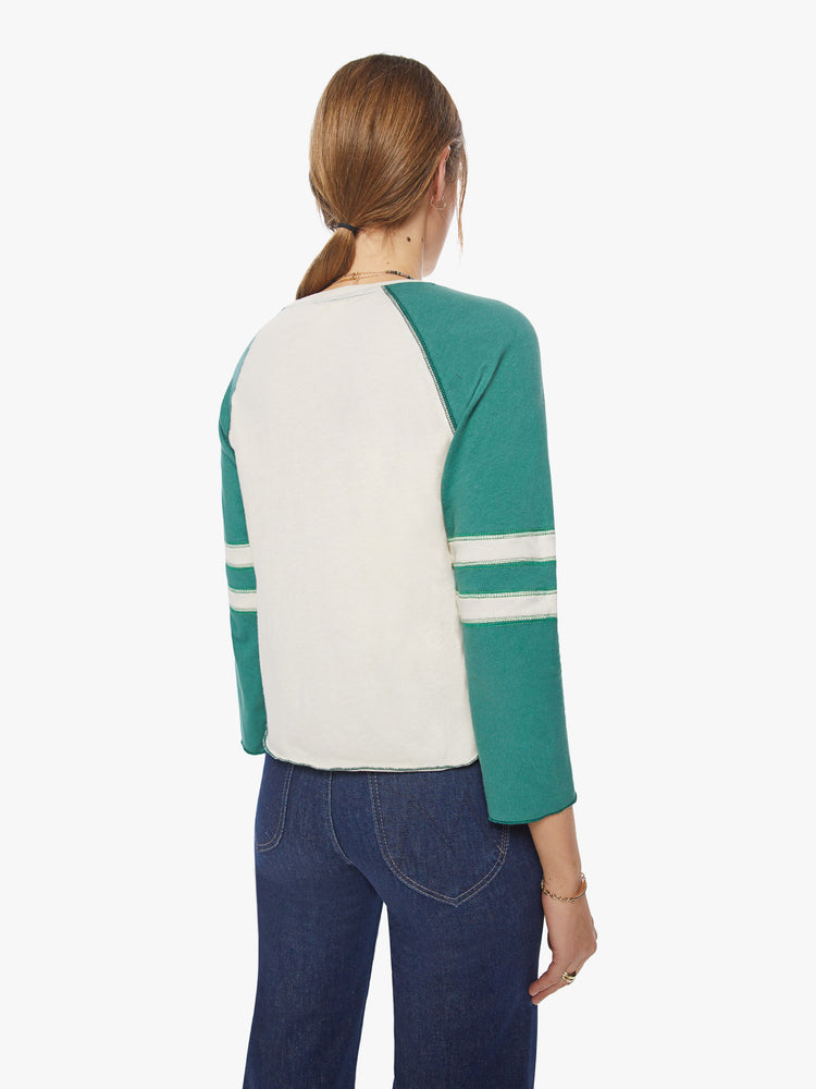 Back view of a woman concert tee designed with a crew neck, 3/4 sleeves in an off-white hue with teal sleeves.