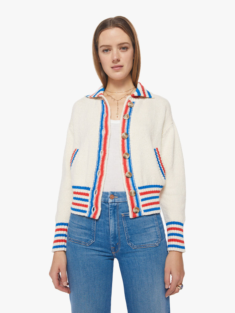 Front view of a woman collared cardigan sweater with drop shoulders, slit pockets, thick ribbed hems and buttons down the front in cream features red and blue striped hems and athletic-inspired knit text and numbers on the back.