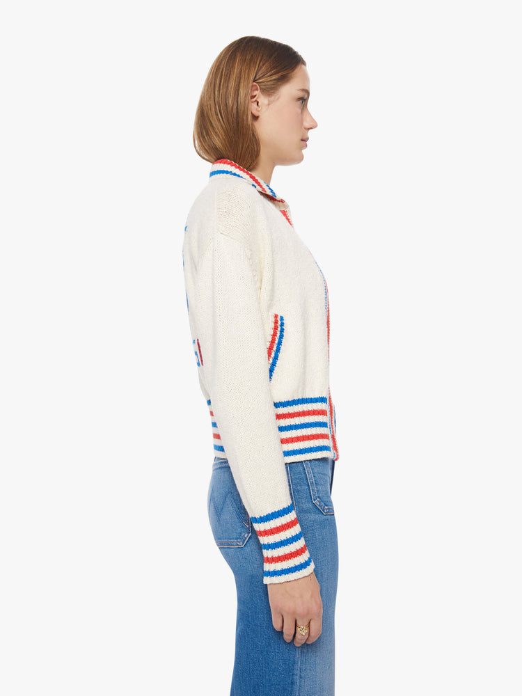 Side view of a woman collared cardigan sweater with drop shoulders, slit pockets, thick ribbed hems and buttons down the front in cream features red and blue striped hems and athletic-inspired knit text and numbers on the back.