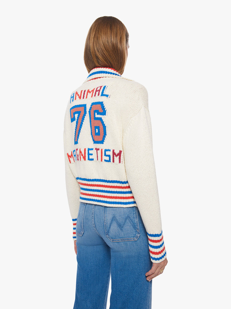 Back view of a woman collared cardigan sweater with drop shoulders, slit pockets, thick ribbed hems and buttons down the front in cream features red and blue striped hems and athletic-inspired knit text and numbers on the back.