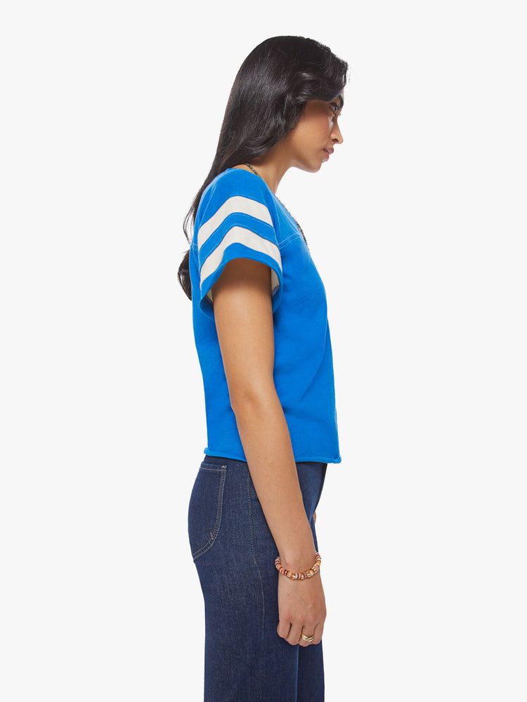 Side view of a woman blue with white stripes on the sleeves football tee with a a V-neck with a seamed detail across the chest, short sleeves, drop shoulders.