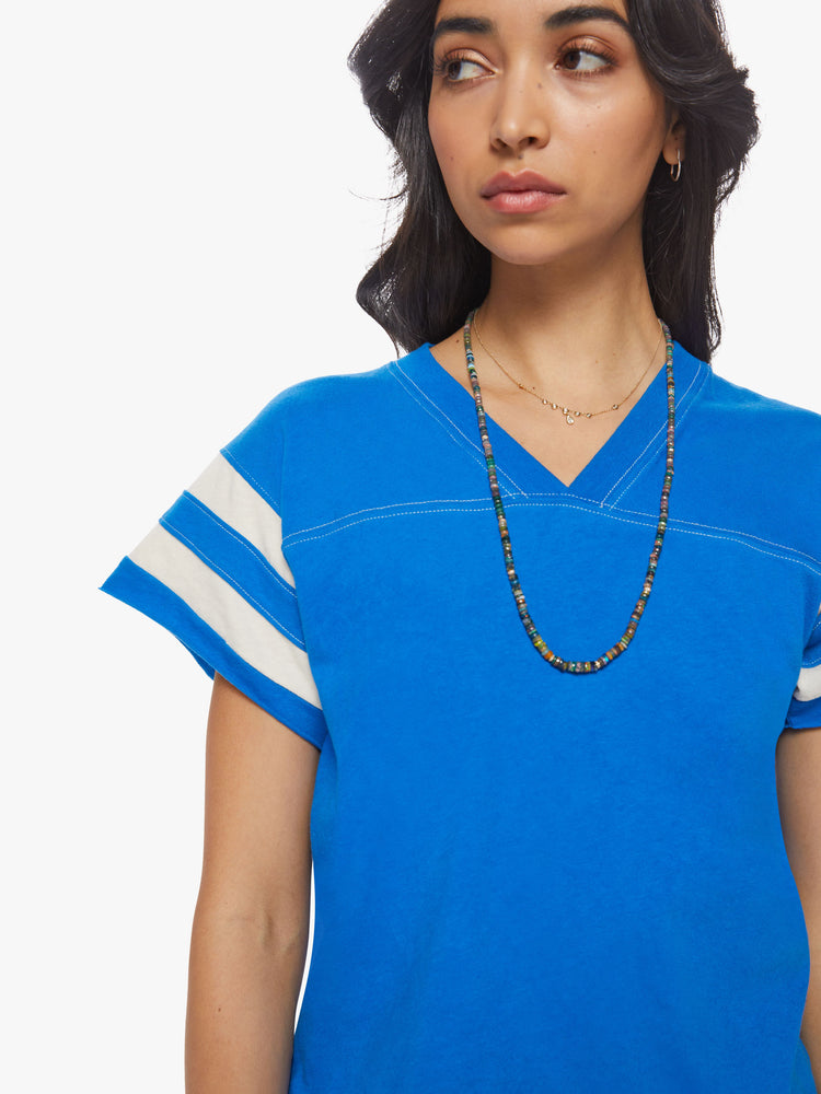 Close up view of a woman blue with white stripes on the sleeves football tee with a a V-neck with a seamed detail across the chest, short sleeves, drop shoulders.