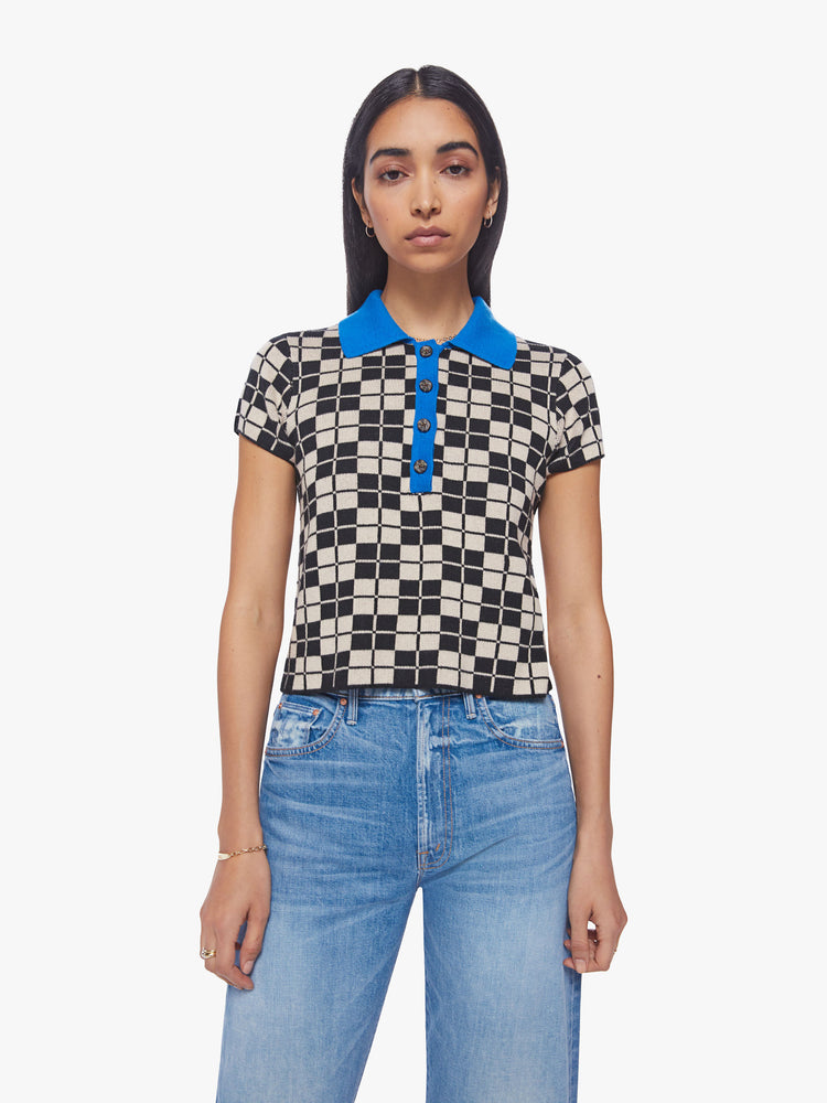 Front view of a woman short sleeve knit polo in a black and cream checkered print with a bright blue collar and button placket.