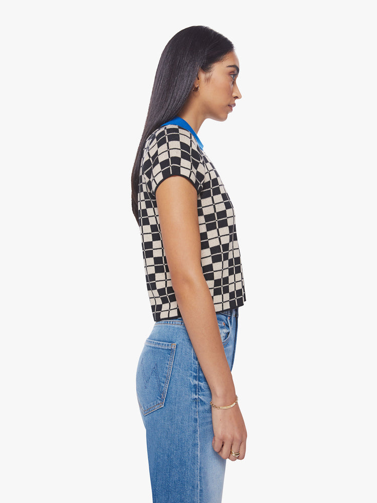Side view of a woman short sleeve knit polo in a black and cream checkered print with a bright blue collar and button placket.
