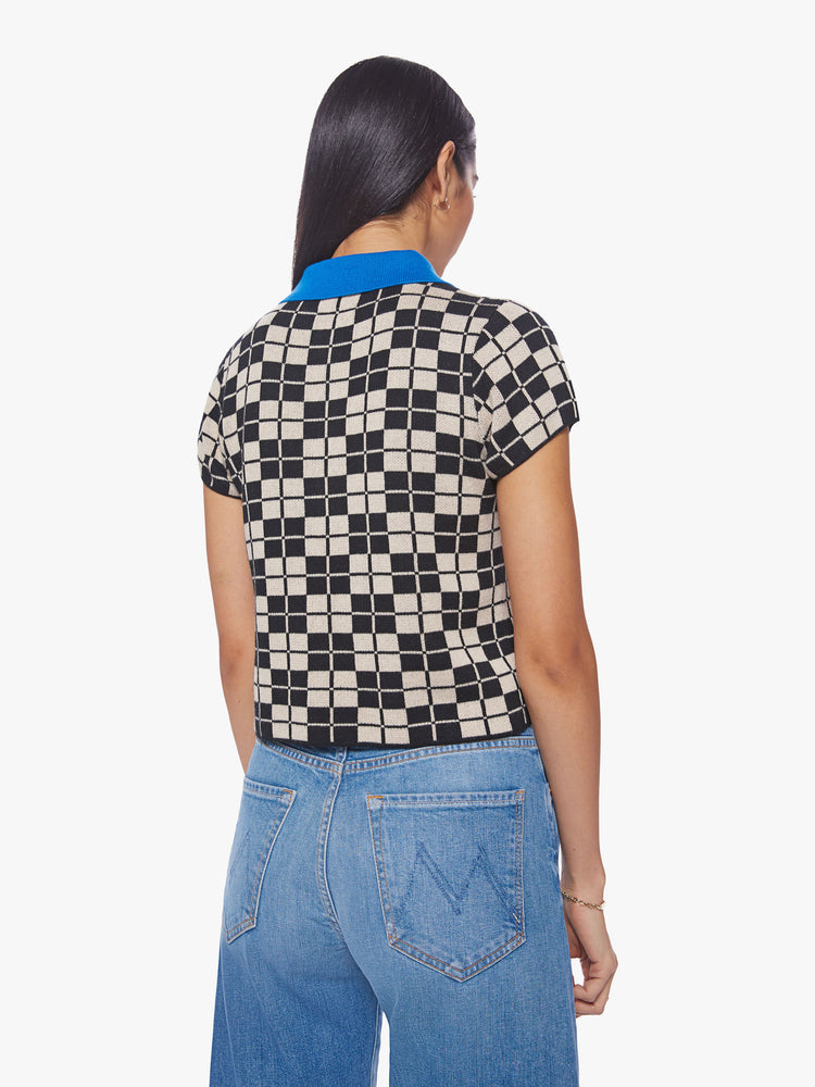 Back view of a woman short sleeve knit polo in a black and cream checkered print with a bright blue collar and button placket.