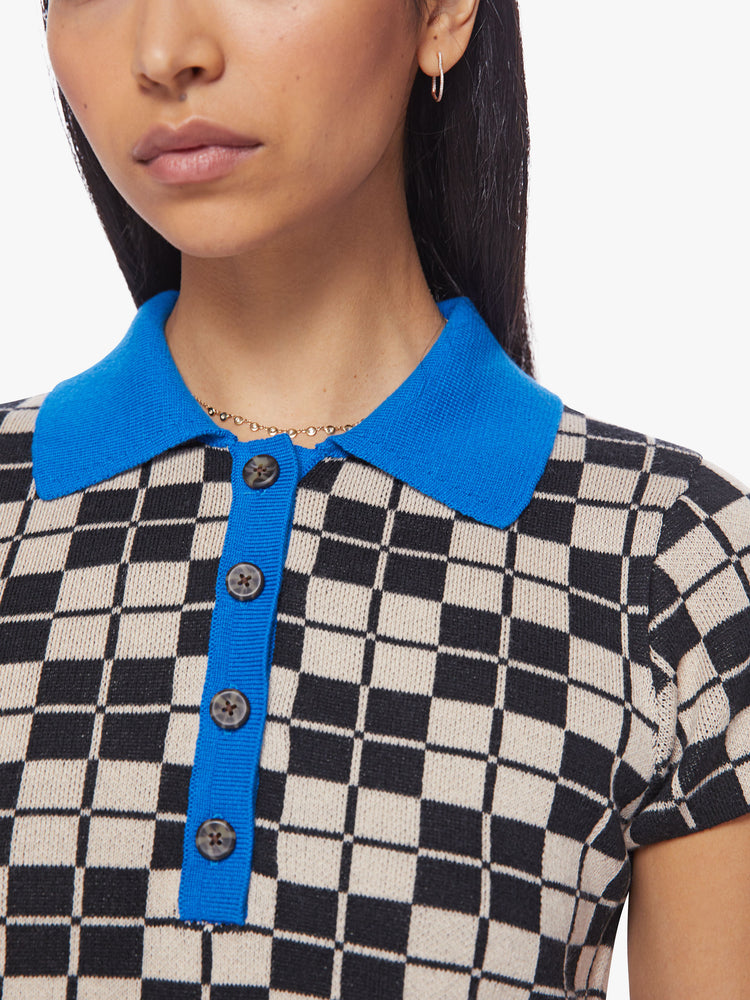 Close up view of a woman short sleeve knit polo in a black and cream checkered print with a bright blue collar and button placket.