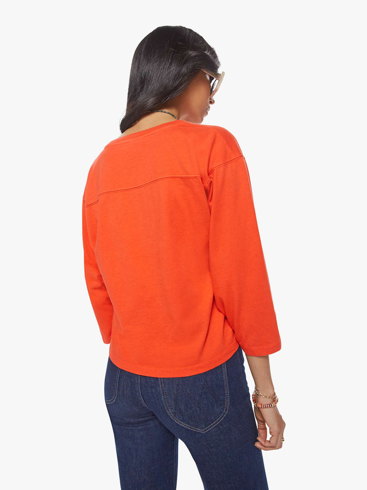 Back view of a woman wearing an orange 3/4 sleeve football shirt with drop shoulders.