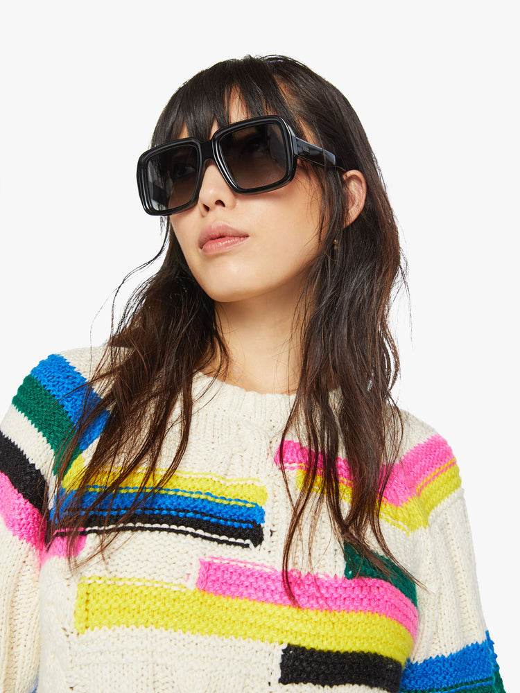 Close up view of a woman crewneck sweater in an off-white with colorful stripes, checks and cable knits details.