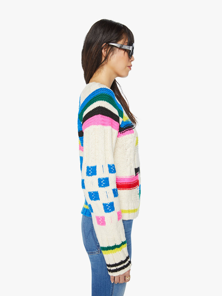 Side view of a woman crewneck sweater in an off-white with colorful stripes, checks and cable knits details.