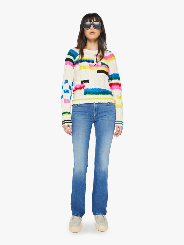 Full body view of a woman crewneck sweater in an off-white with colorful stripes, checks and cable knits details.