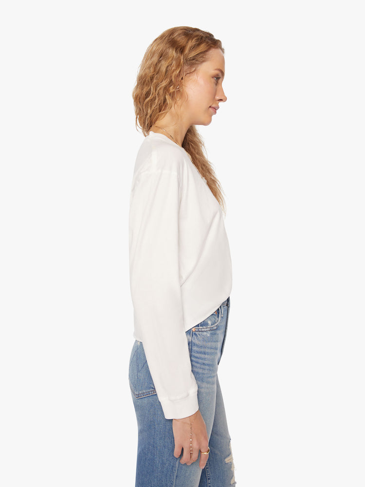 Side view of a womens white crew neck shirt featuring cuffed long sleeves and a raw cropped hem.
