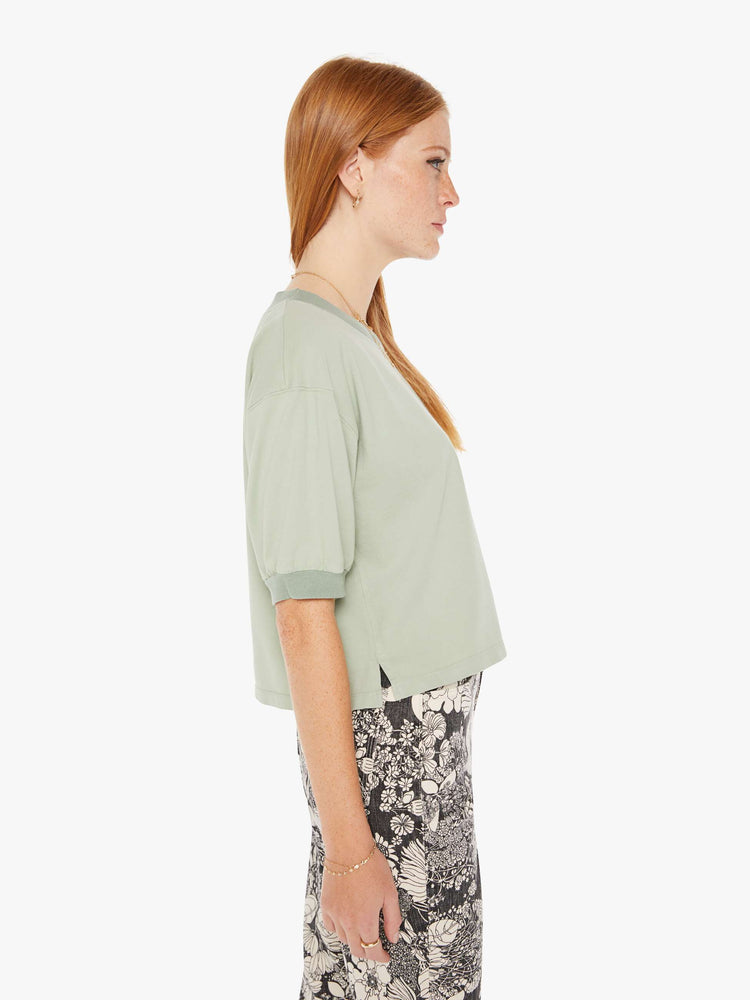 Side view of a womens faded green shirt featuring ribbed hems and puff sleeves.