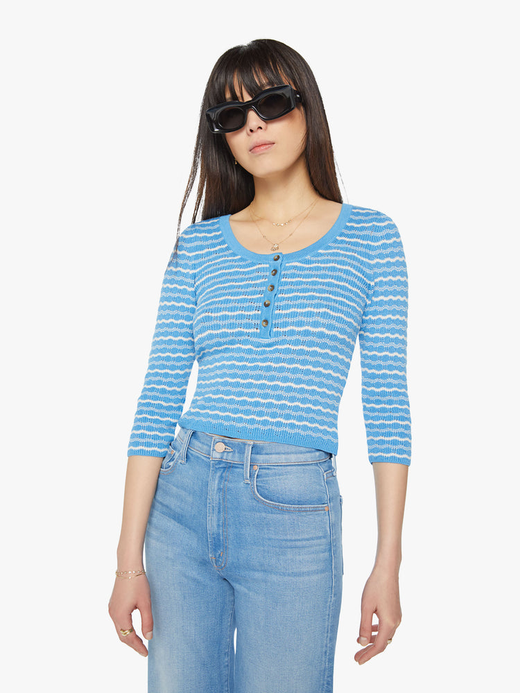 Front view of a woman cropped henley with a buttoned scoop neck, 3/4-length sleeves and a slightly shrunken fit in a baby blue and white stripe pattern.