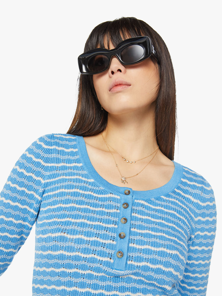 Close up view of a woman cropped henley with a buttoned scoop neck, 3/4-length sleeves and a slightly shrunken fit in a baby blue and white stripe pattern.