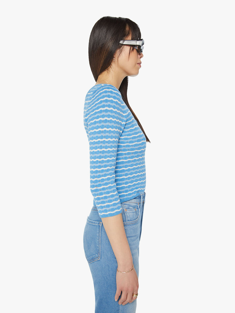 Side view of a woman cropped henley with a buttoned scoop neck, 3/4-length sleeves and a slightly shrunken fit in a baby blue and white stripe pattern.