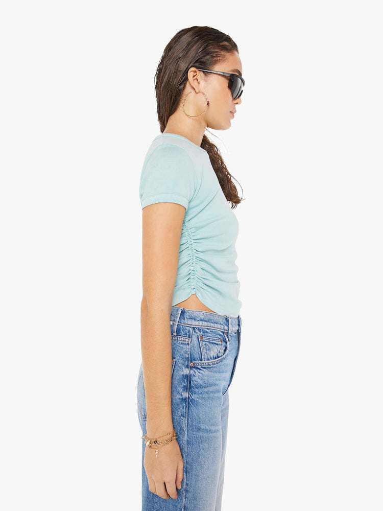 Side view of a woman wearing am eggshell blue crew neck tee featuring cinched side seams, paired with a medium blue wash jean.