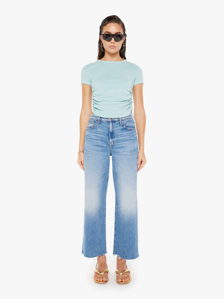 Front full body view of a woman wearing am eggshell blue crew neck tee featuring cinched side seams, paired with a medium blue wash, wide leg jeans.
