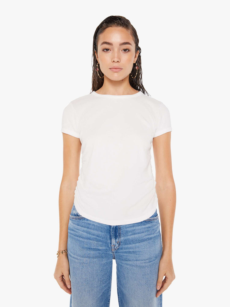 Front view of a woman wearing a white crew neck tee featuring cinched side seams, paired with a medium blue wash jean.