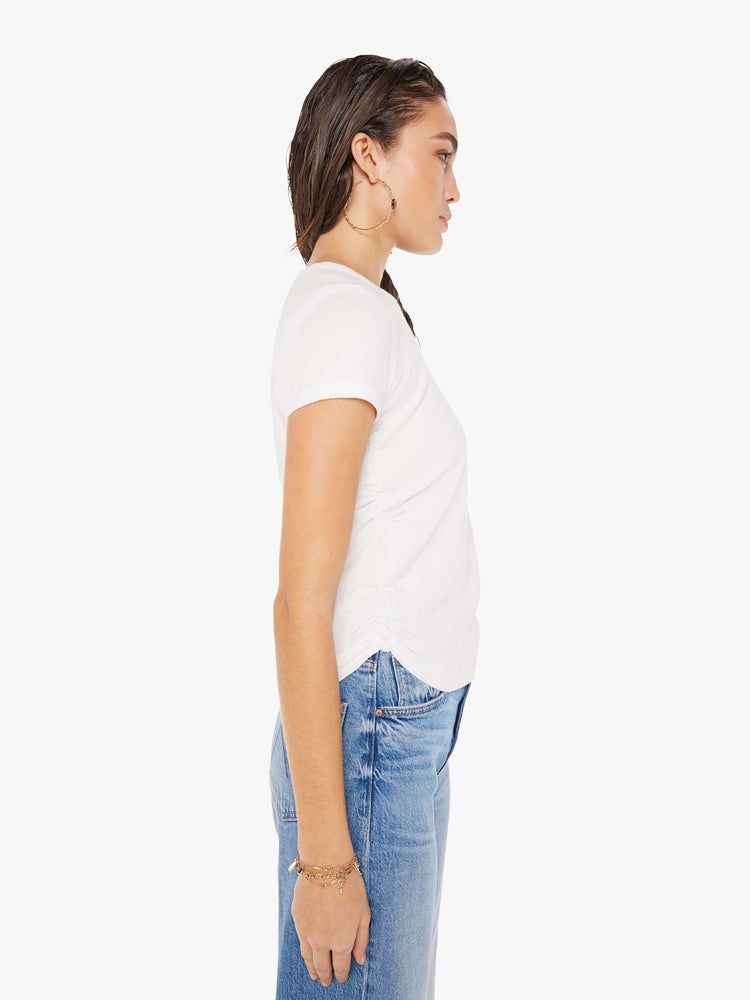 Side view of a woman wearing a white crew neck tee featuring cinched side seams, paired with a medium blue wash jean.