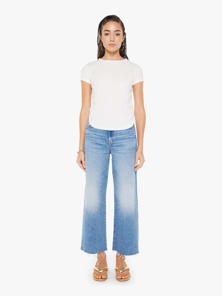 Front full body view of a woman wearing a white crew neck tee featuring cinched side seams, paired with a medium blue wash, wide leg jean.