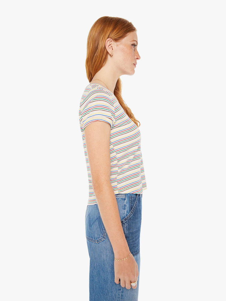 Side view of a woman baby tee with a V-neck, short sleeves and a slim fit in white with rainbow stripes throughout.