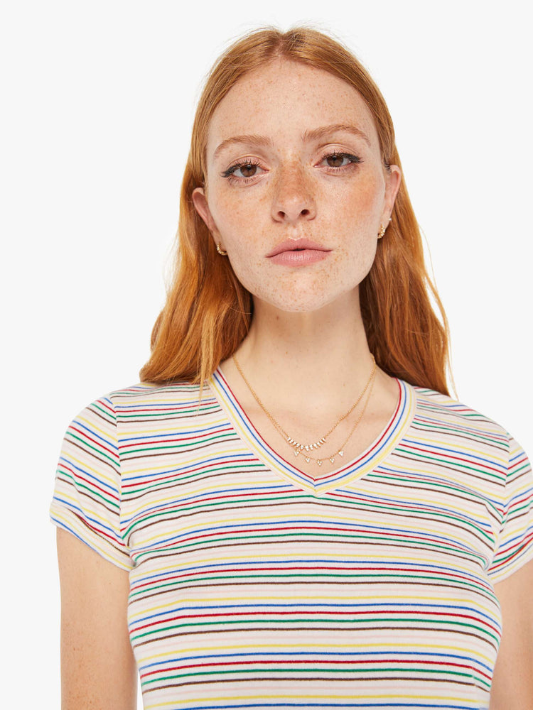 Close up view of a woman baby tee with a V-neck, short sleeves and a slim fit in white with rainbow stripes throughout.