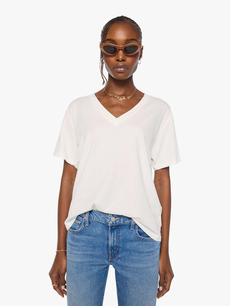 Front view of a woman in an off white  V-neck tee with drop shoulders and a loose, boxy fit. 