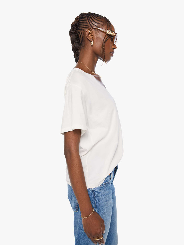 Side view of a woman in an off white  V-neck tee with drop shoulders and a loose, boxy fit. 