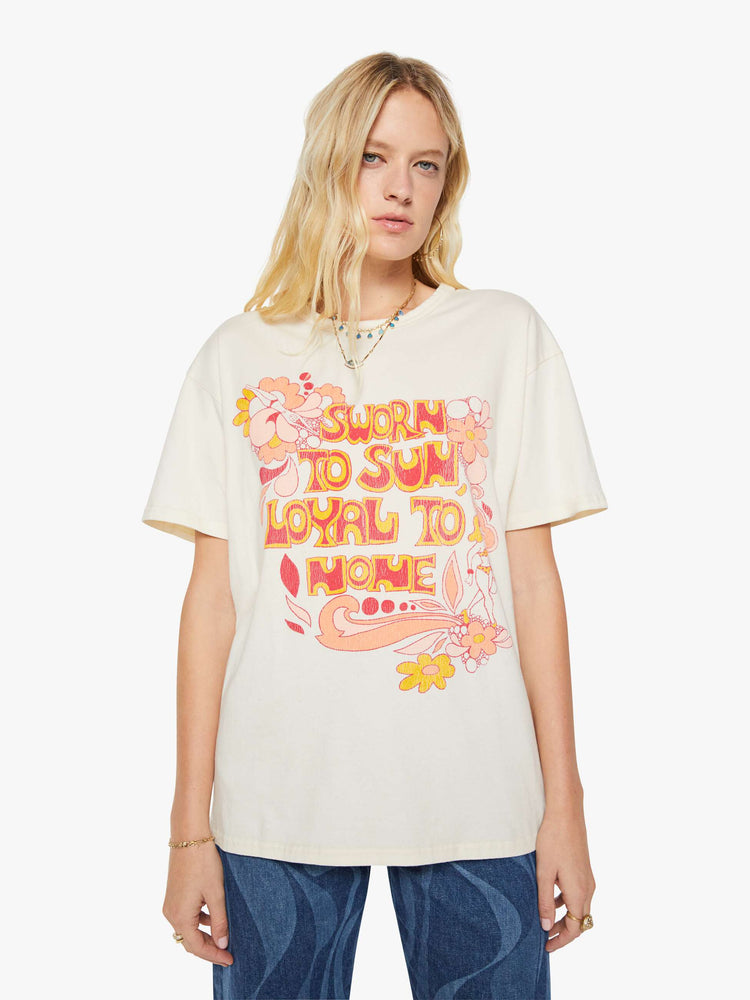 Front view of a woman in a white oversized tee with a crackled text graphic with flowers and swimmers on the front.