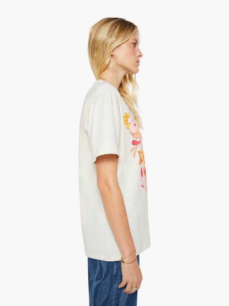 Side view of a woman in a white oversized tee with a crackled text graphic with flowers and swimmers on the front.