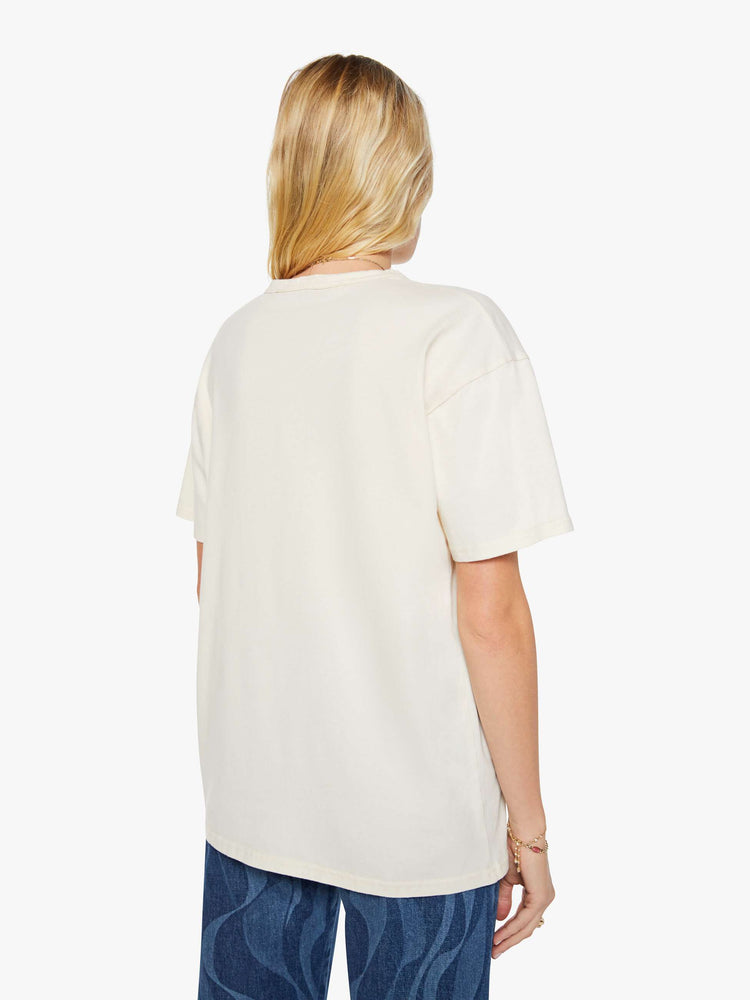 Back view of a woman in a white oversized tee with a crackled text graphic with flowers and swimmers on the front.