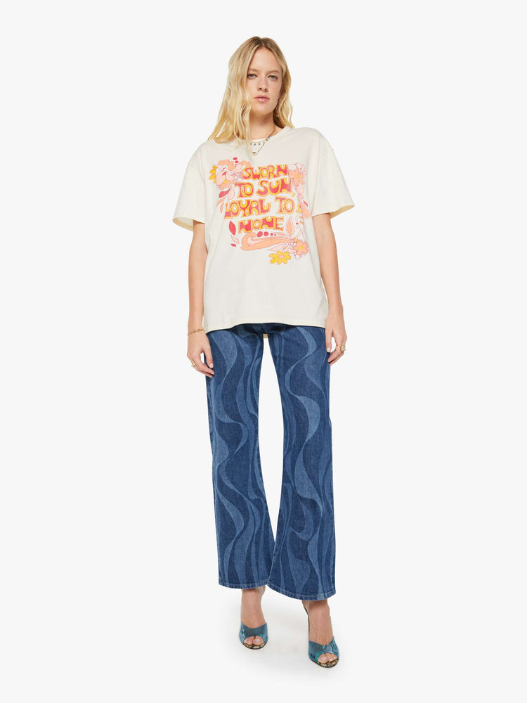 Full body view of a woman in a white oversized tee with a crackled text graphic with flowers and swimmers on the front.