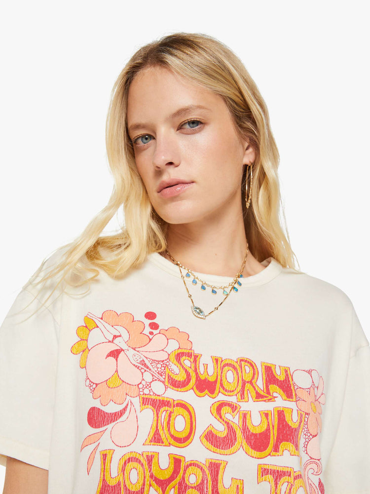 Close up view of a woman in a white oversized tee with a crackled text graphic with flowers and swimmers on the front.