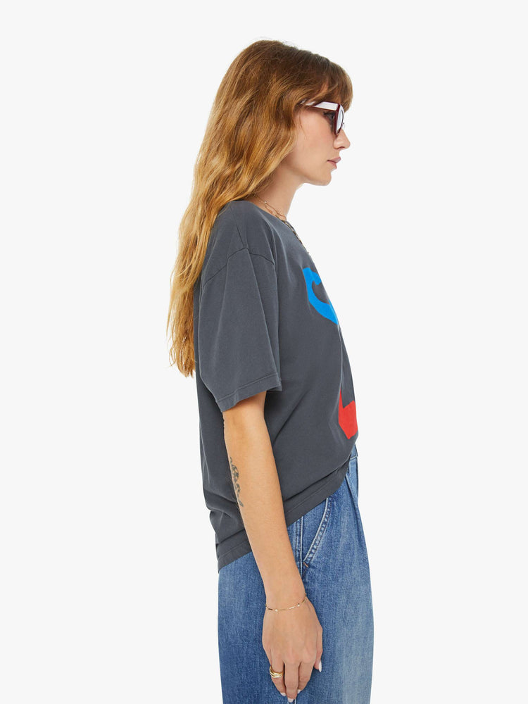 Side view of a woman dark grey tee with a red and blue text graphic on the front.