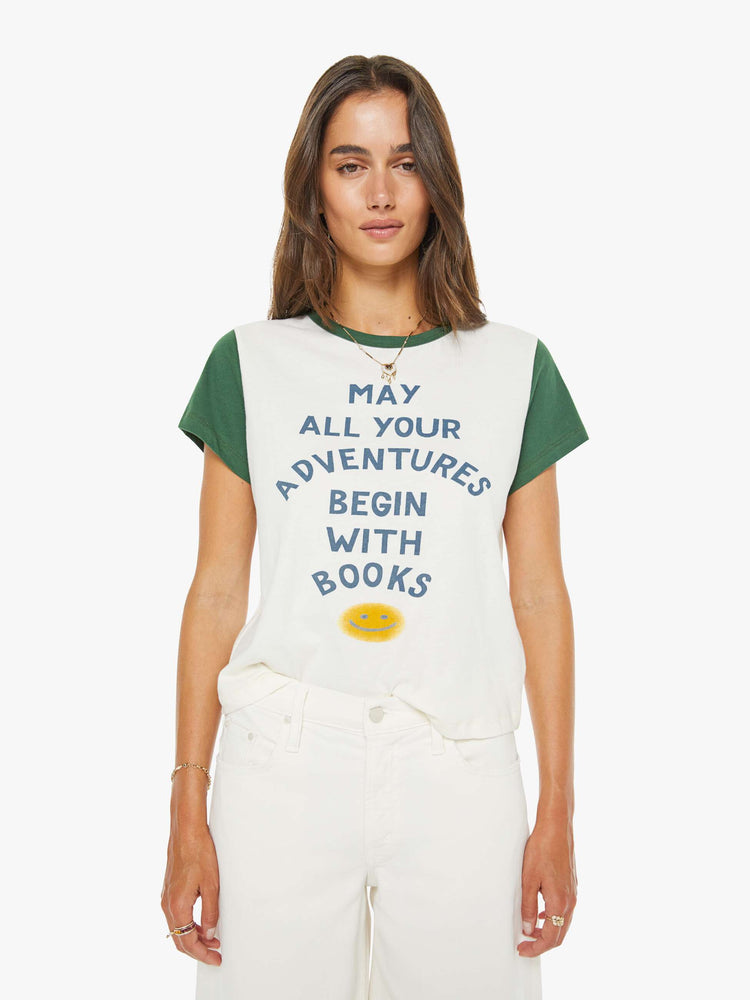 Front view of a woman in off-white with green trim tee features blue block text and a smiley face graphic on the front.